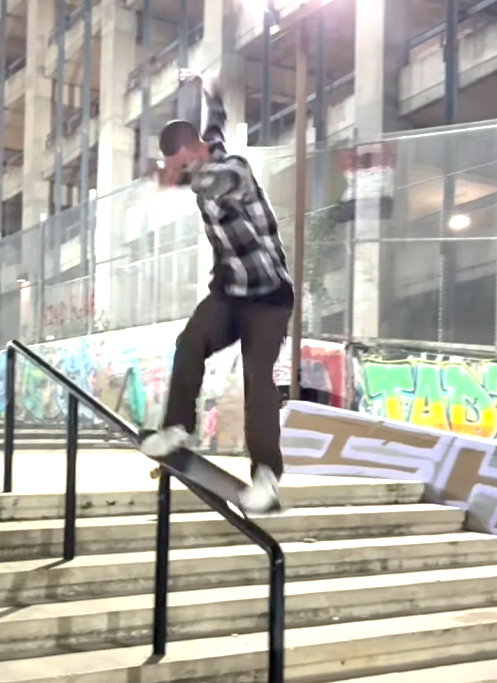 A skater named Trenton grinding a metal handrail at a skatepark, knees bent, board locked in place, sparks of motion around him with concrete and park features in the background.